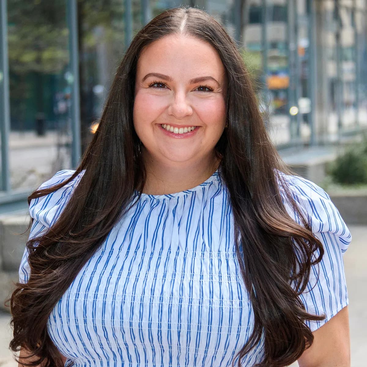 Amy Molina smiling in a blue top against an outdoor urban background.