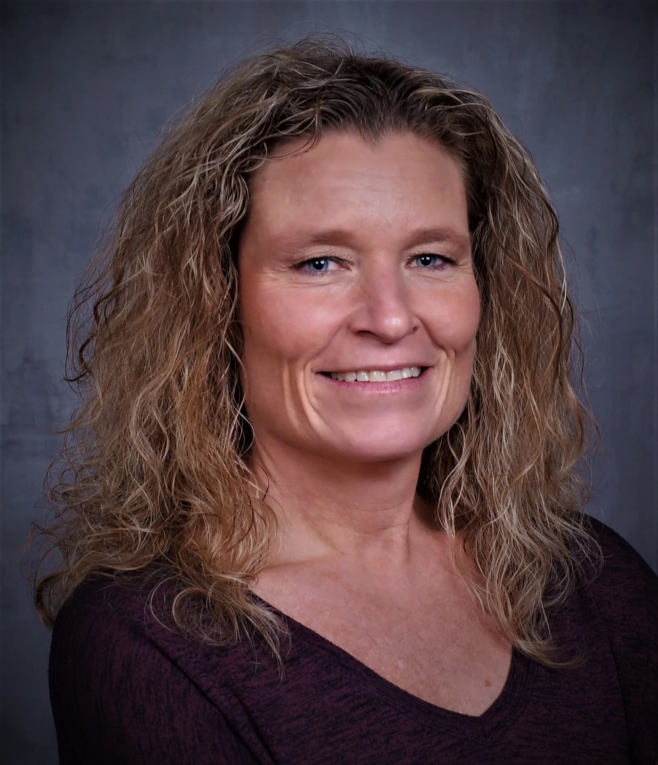 Kerri Wirachowsky smiling in a purple sweater against a gray office background.