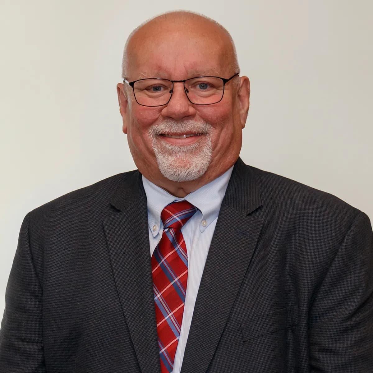 Kevin Hogan smiling in a gray blazer and red tie against a white office background.