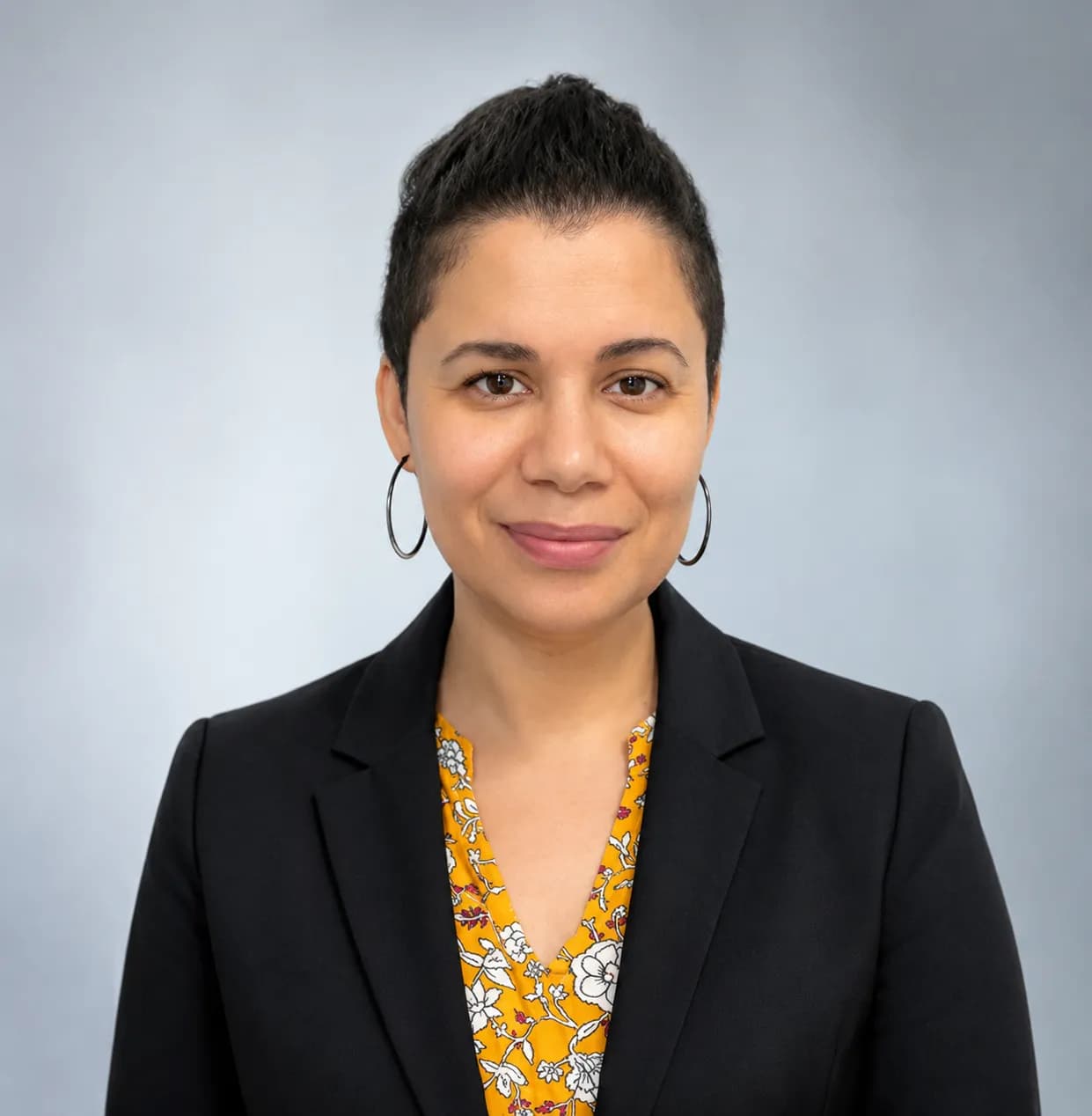 Nicole Leandro smiling in a black blazer against a gray office background.