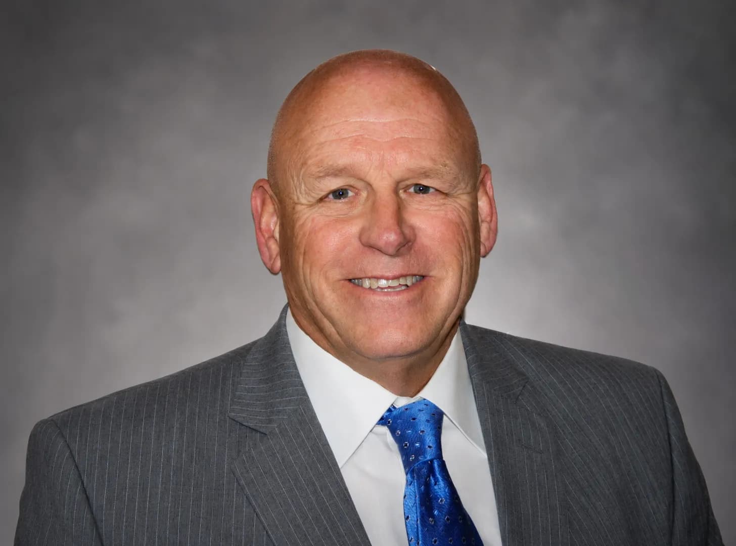 Terry Kummer smiling in a grey blazer and blue tie against a gray office background.
