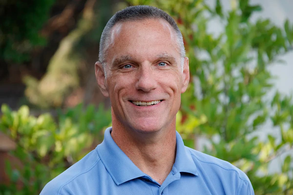 Terry Moore smiling in a bluepolo against a outdoor tree line background.