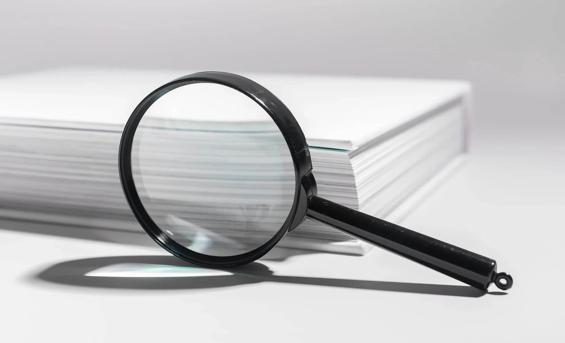 A magnifying glass over a tall stack of papers