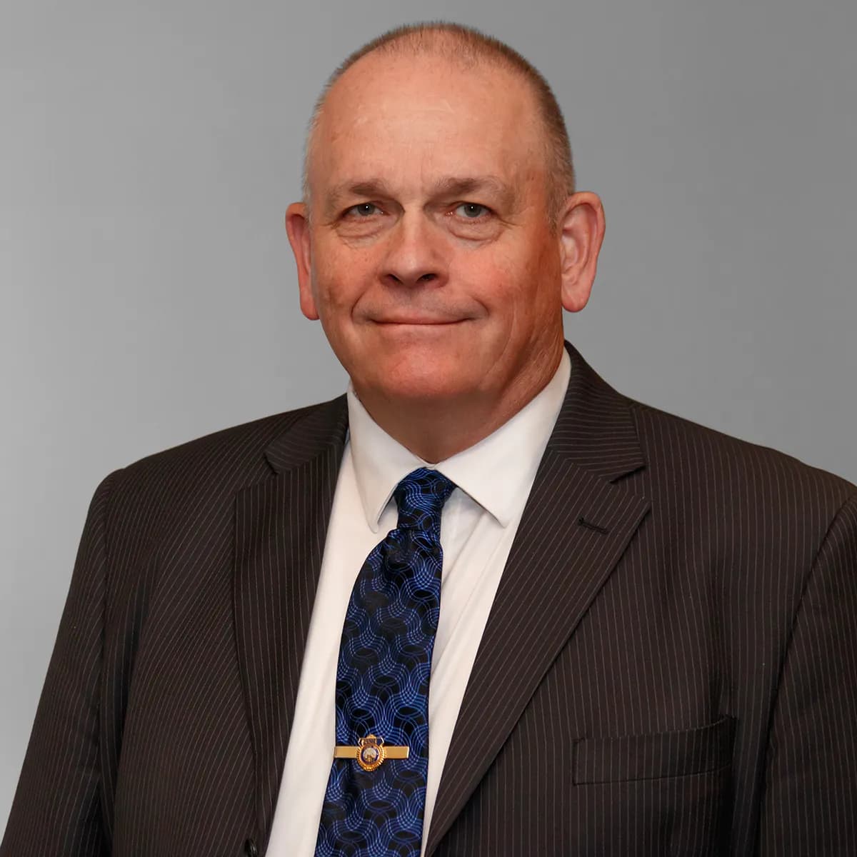 Bill Reese smiling in a blazer and tie against a gray office background.