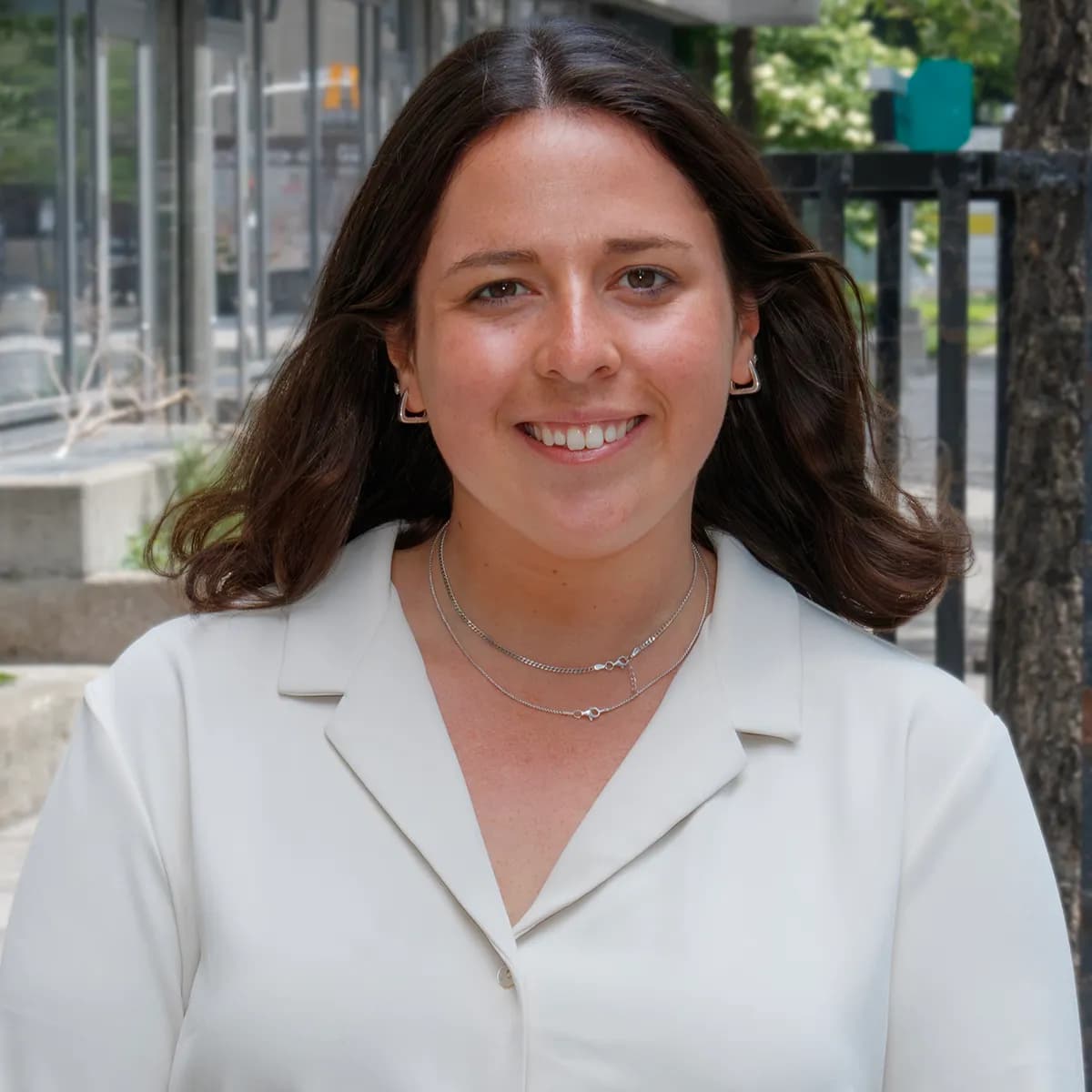 Madeleine Winslow smiling in a white blazer against an outdoor urban background.