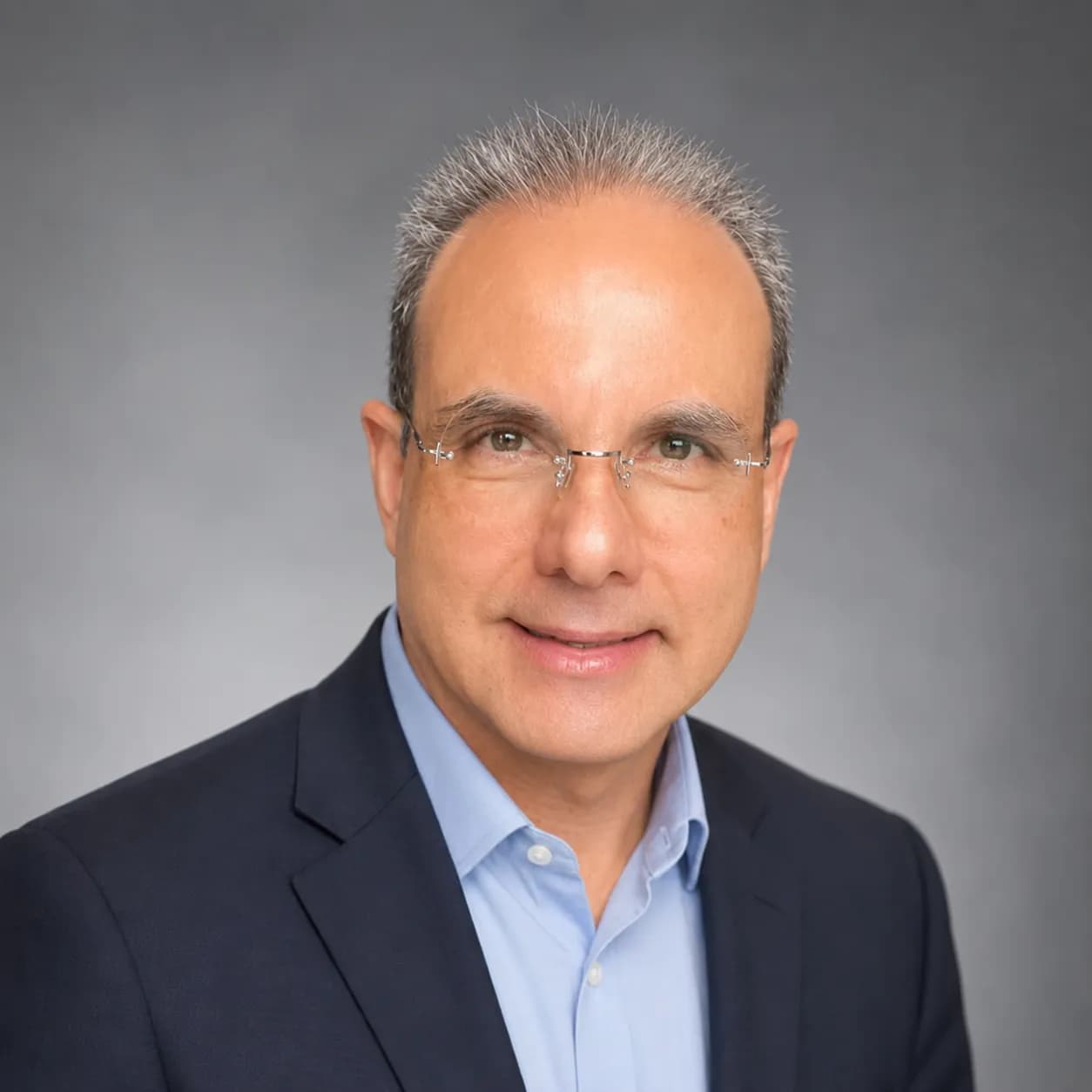 Rodolfo Giacoman smiling in a blue blazer against a gray office background.